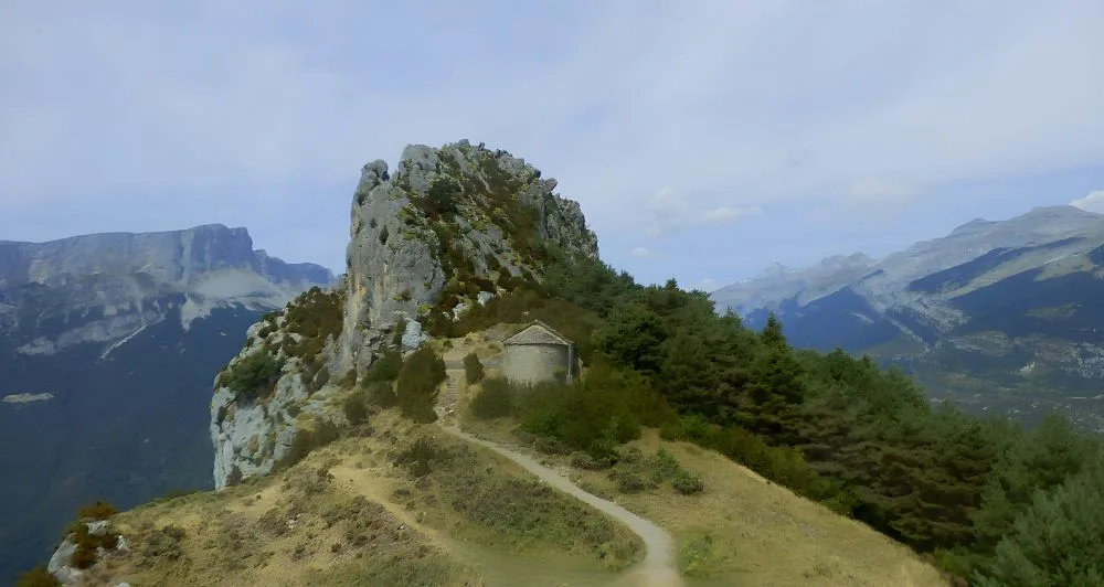 Hermitage of Saint John and Saint Paul, Tella, Huesca, Spain. The image showcases a small Romanesque stone chapel perched on a rugged hilltop in the Pyrenees.