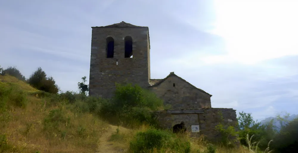 The Hermitage of the Virgin of the Fajanillas, Tella, Huesca, Spain – The Land of the Witches." The image showcases a serene medieval stone chapel set amidst the breathtaking Pyrenean landscape.