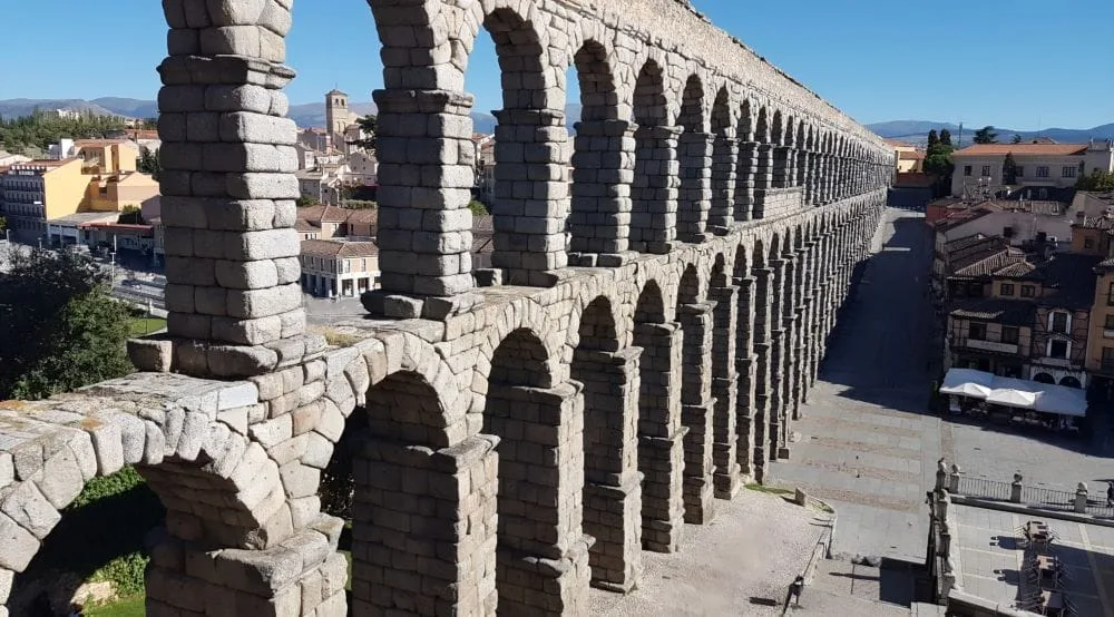 The Roman Aqueduct of Segovia, Spain, an iconic structure dating back to the 1st century AD. The aqueduct, made of large stone blocks without mortar, spans across the city, featuring two tiers of arches that rise gracefully above the landscape.