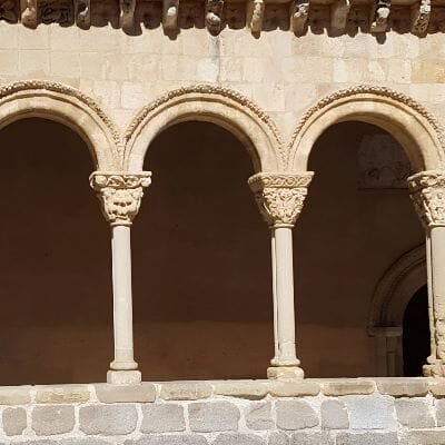 The southern gallery of the Church of San Lorenzo in Segovia, Spain, built during the 12th and 13th centuries. The Romanesque gallery features a series of pointed arches supported by slender columns, with intricate stone carvings adorning the structure.