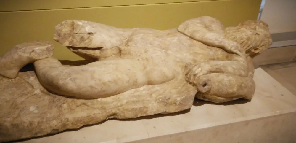 Silent Guardian of Eternity: A funerary sculpture from Baelo Claudia depicts a wise, bearded old man in eternal repose upon a lion's pelt, a symbol of his journey into the afterlife.