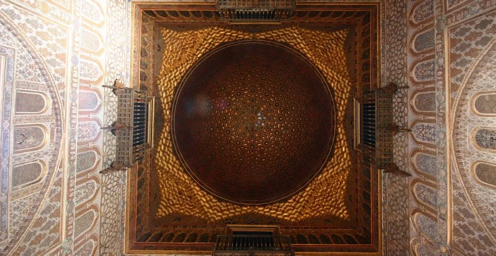 The resplendent Mudéjar dome of the Salón de Embajadores at the Alcázar of Seville, crafted by Diego Ruiz in 1427, symbolizing the cosmos in a harmonious blend of cultural artistry.