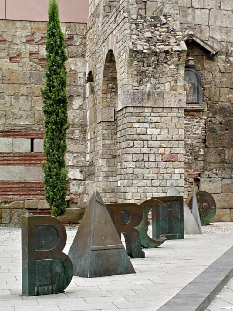 Vestiges of Barcelona's Roman aqueduct, a testament to the city's ancient engineering marvels, stand in harmony with Joan Bossà's 'Barcino' sculpture, bridging history with modern artistry.