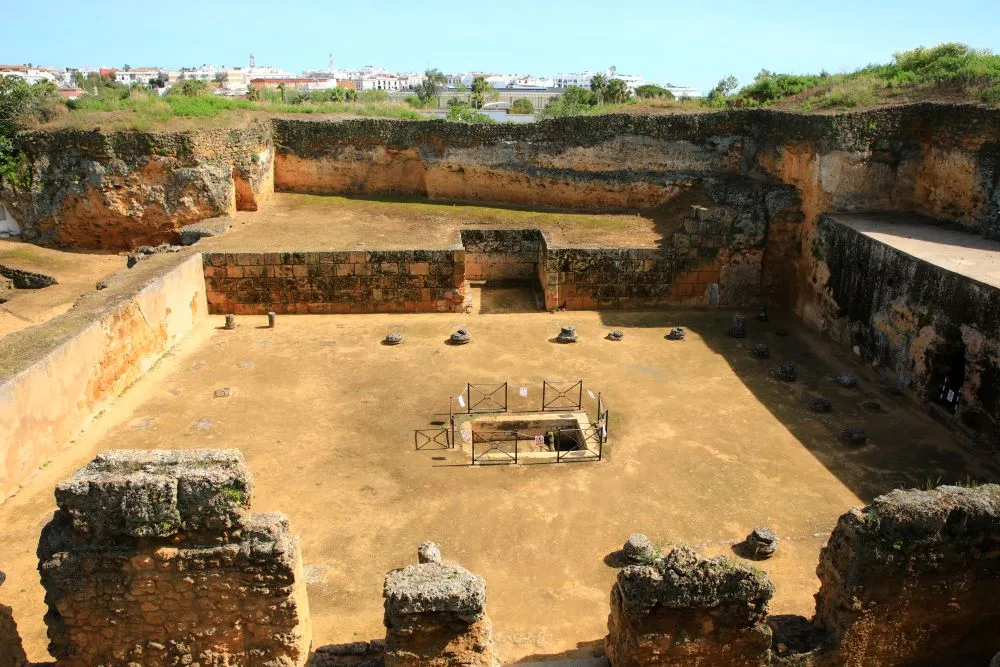 Photograph of the Tomb of Servilia in the Roman necropolis of Carmona, Andalusia, Spain. The image showcases the intricate architecture of one of the best-preserved Roman ruins in Spain, highlighting the historical significance of Spanish Roman ruins. The tomb is surrounded by ancient stonework and lush greenery, offering a glimpse into the region's rich Roman heritage.