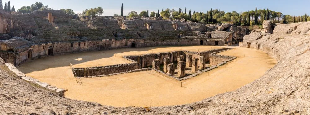 View of the Amphitheater in the ancient Roman city of Italica, located in Santiponce, Seville, Spain. This edited photograph highlights the remarkable architecture and scale of one of the best-preserved Roman ruins in Spain. A prime example of Spanish Roman ruins, the amphitheater showcases the grandeur of Roman engineering and its historical significance in Andalusia.