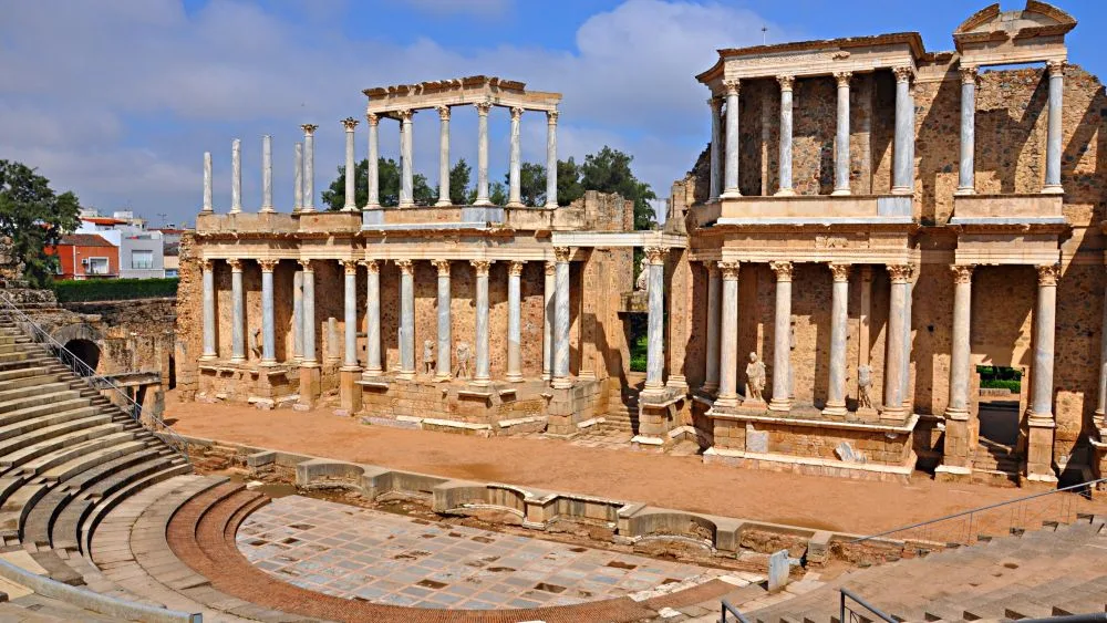 View of the Roman Theatre in Mérida, Extremadura, Spain, featuring semicircular stone seating, a grand stage backdrop with Corinthian columns, and clear blue skies above—one of the best-preserved Roman ruins in Spain.