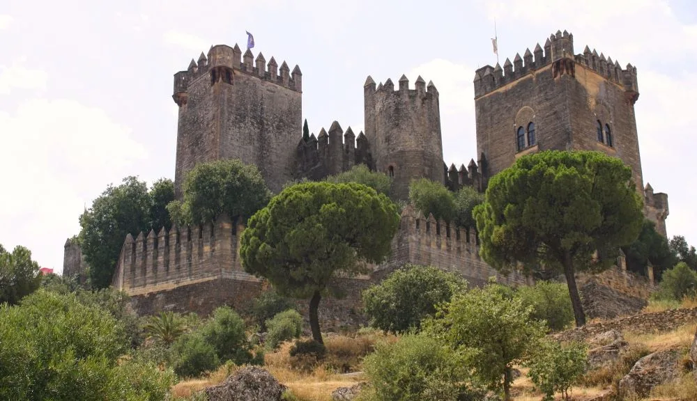 This edited photograph showcases the majestic Castle of Almodóvar del Río, located in the province of Córdoba, Andalusia. The castle, perched on a hilltop, offers panoramic views of the surrounding countryside. The image captures the historical architecture of the castle, with its imposing towers and fortified walls, set against a clear sky and lush green landscape. The photograph highlights the castle's strategic location and its importance in the region's history.