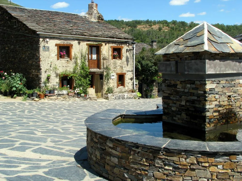 The central fountain in the main square of Valverde de los Arroyos, Spain, surrounded by traditional black slate buildings, creating a picturesque and historic village setting.