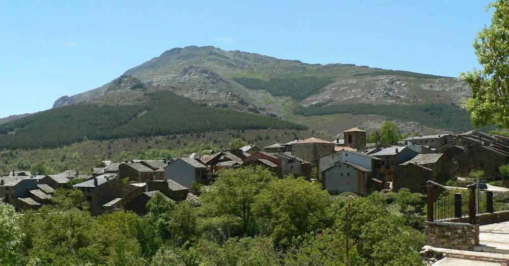 A scenic view of Valverde de los Arroyos, Spain, showcasing the village’s traditional black slate architecture nestled within the natural beauty of the Sierra Norte mountains. The image captures the charm and authenticity of this historic rural enclave.