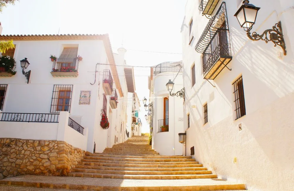 A scenic view of Altea, Alicante, Spain, featuring its charming whitewashed buildings, narrow streets, and the iconic blue-domed church, set against a coastal Mediterranean backdrop.