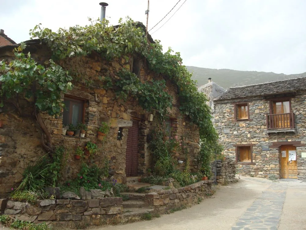 A scenic view of Valverde de los Arroyos, Spain, showcasing its traditional black slate architecture, stone-paved streets, and the surrounding natural landscape of the Sierra Norte.