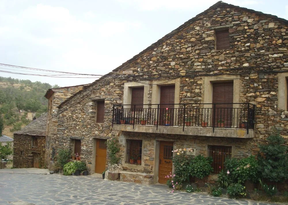 Scenic view of Valverde de los Arroyos, Spain, featuring traditional black slate houses nestled among lush greenery and mountainous landscapes.